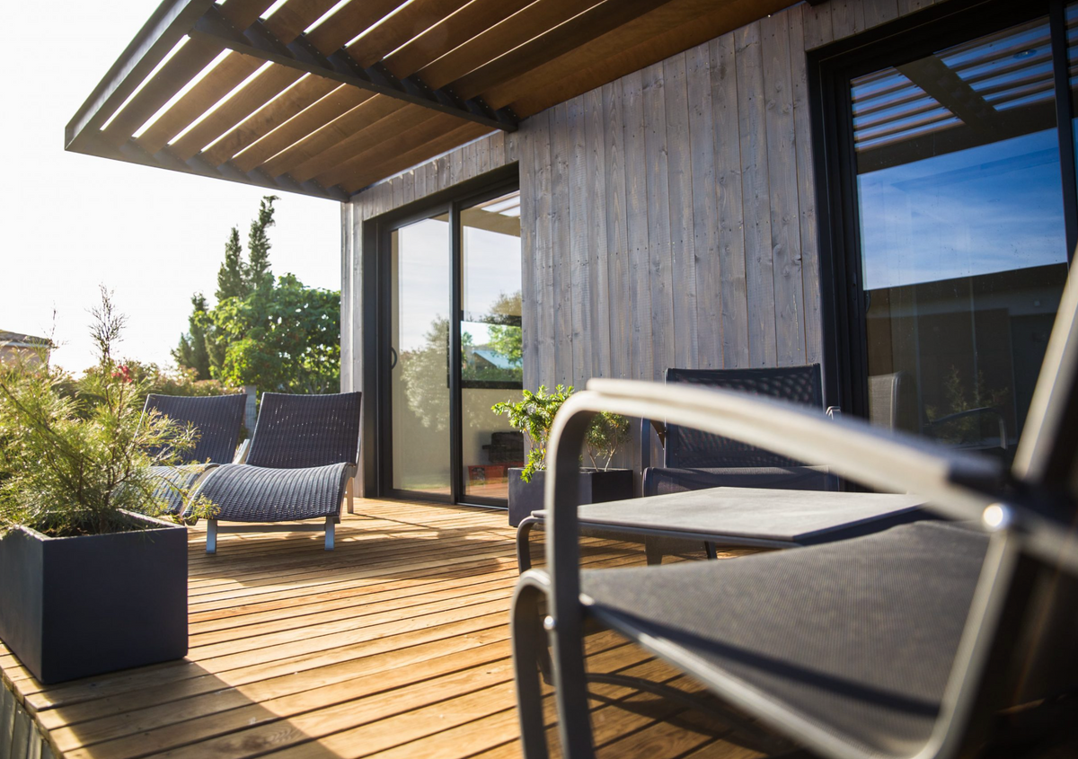 Terrasse en bois d'un studio container sous pergola, bains de soleil et table de jardin