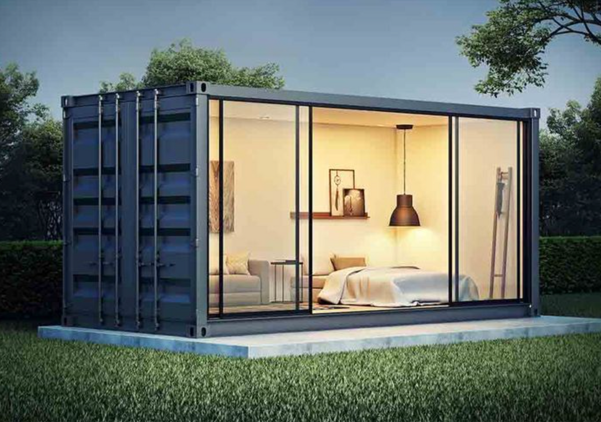 Container aménagé en studio, façade entièrement vitrée éclairée le soir sur une pelouse