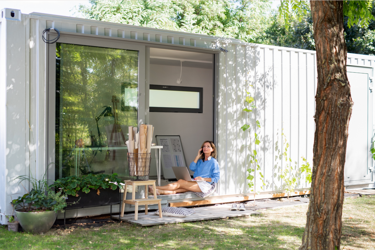 Femme en télétravail installée à la porte d'un container blanc aménagé en bureau de jardin