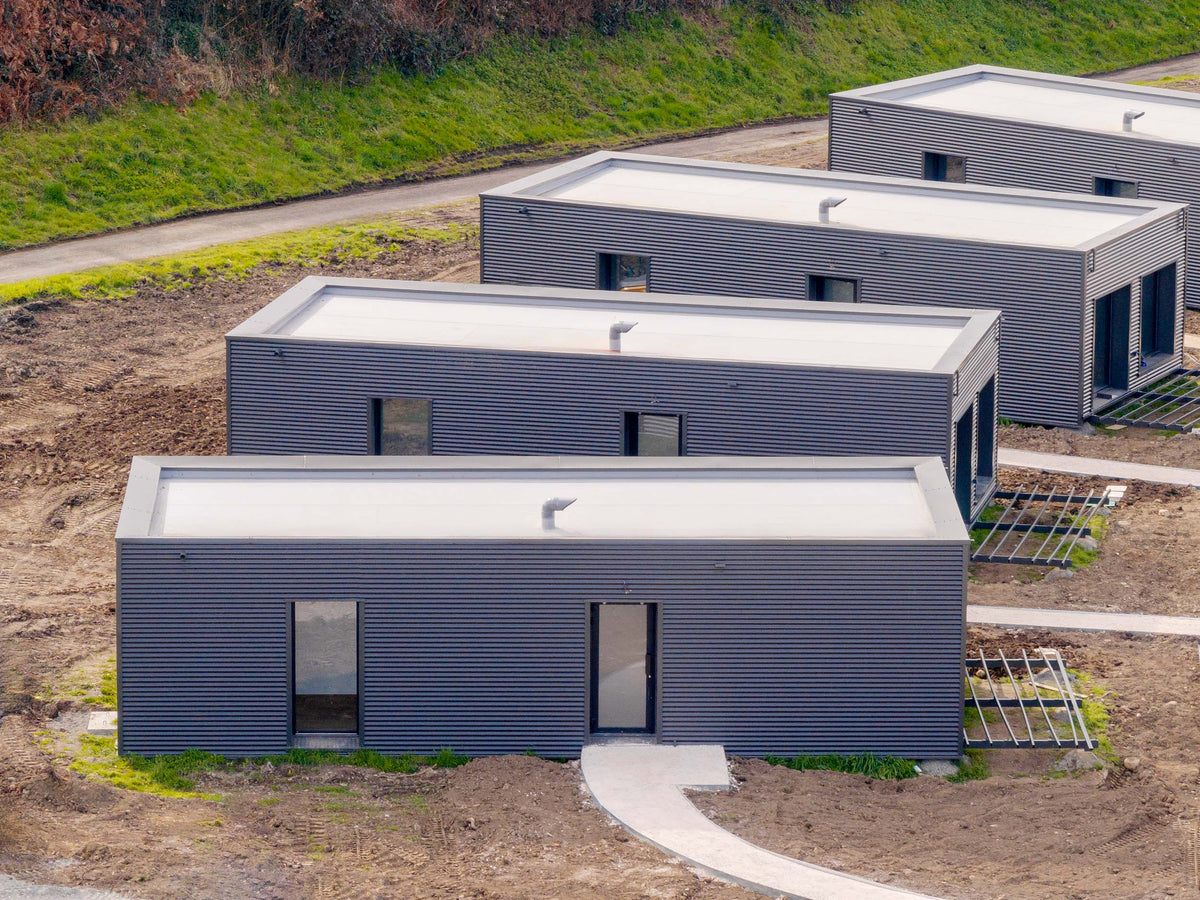 Quatre lodges en containers alignés sur un terrain en pente, bardage bois grisé et toiture plate