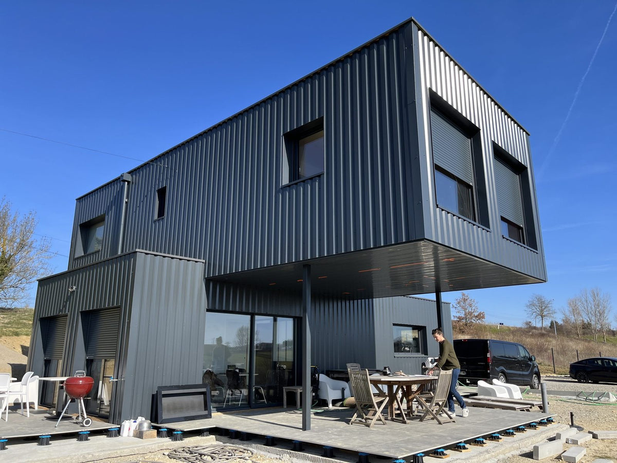 Bâtiment professionnel en containers maritimes à Nailloux, étage en porte-à-faux soutenu par des poteaux métalliques au-dessus de la terrasse couverte