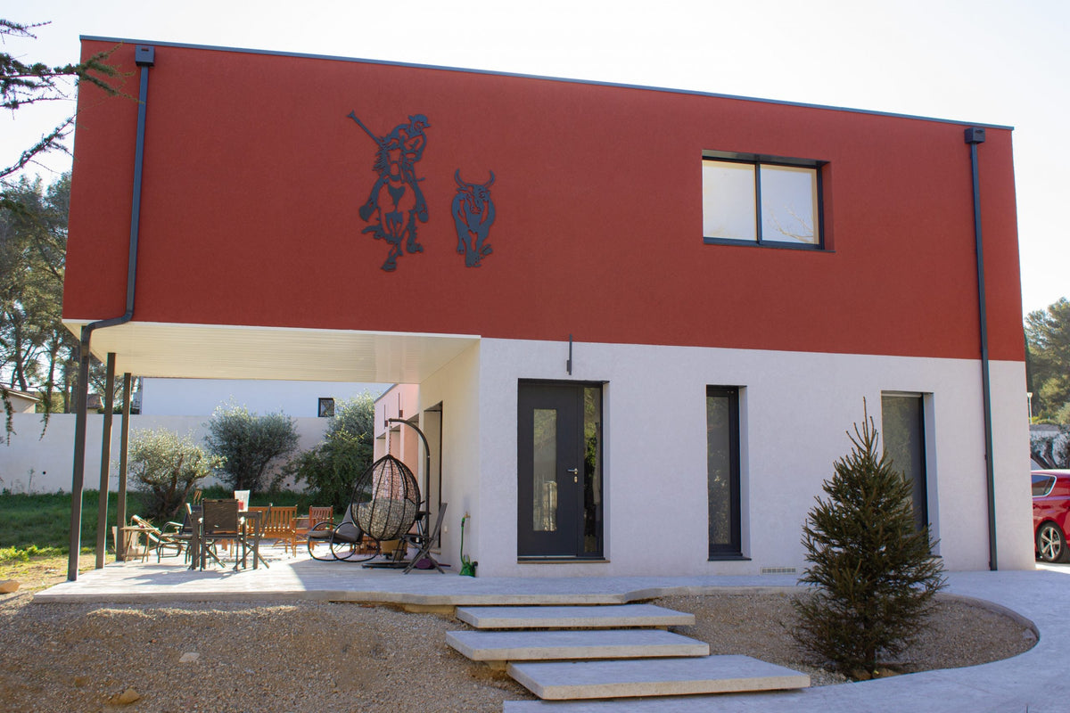 Façade d'entrée de la maison container de Langlade, taureau et gardian de Camargue en acier découpé sur l'enduit rouge