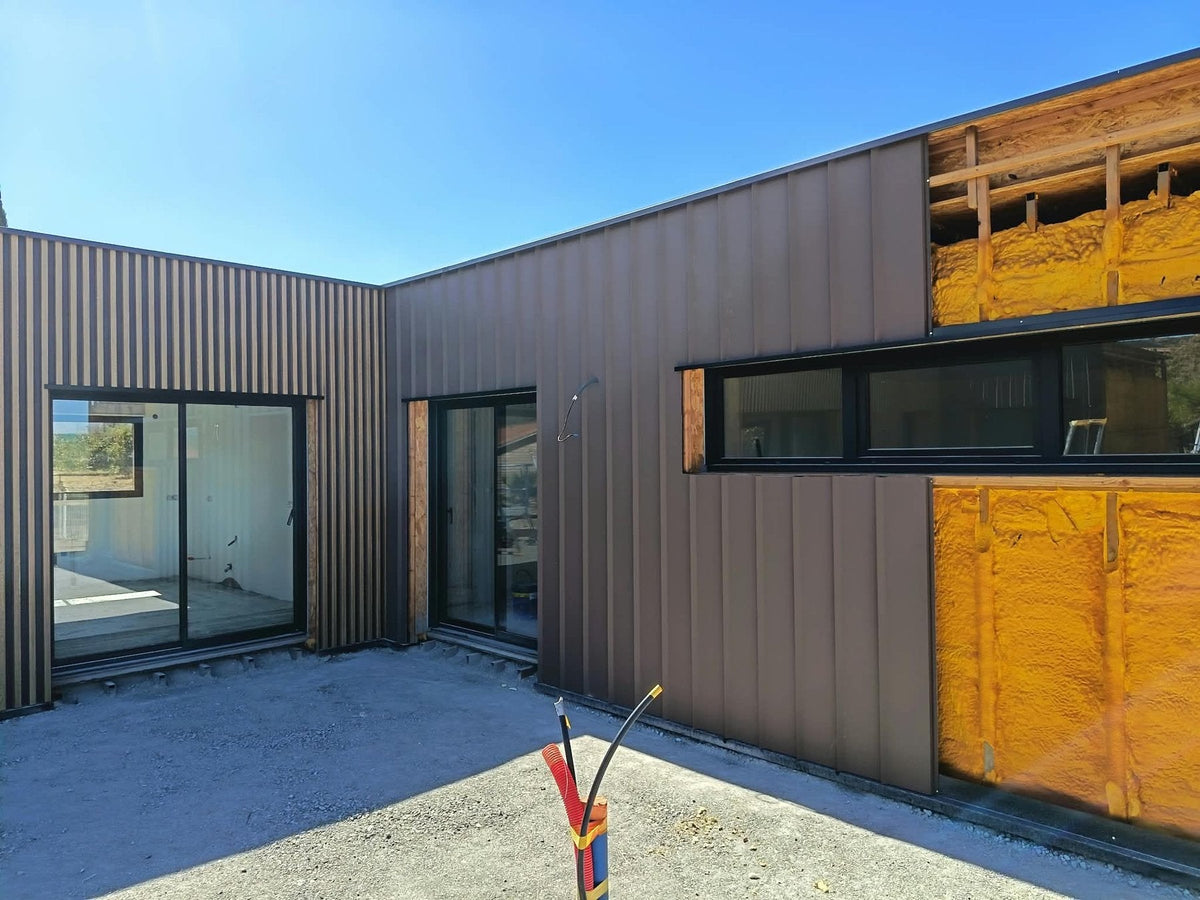 Angle de la maison container de Taurize, bardage acier aspect bois ONWOOD sur le volume de gauche et bardage à joint debout EPURE teinte Volcano à droite, une partie de mur encore en isolation projetée