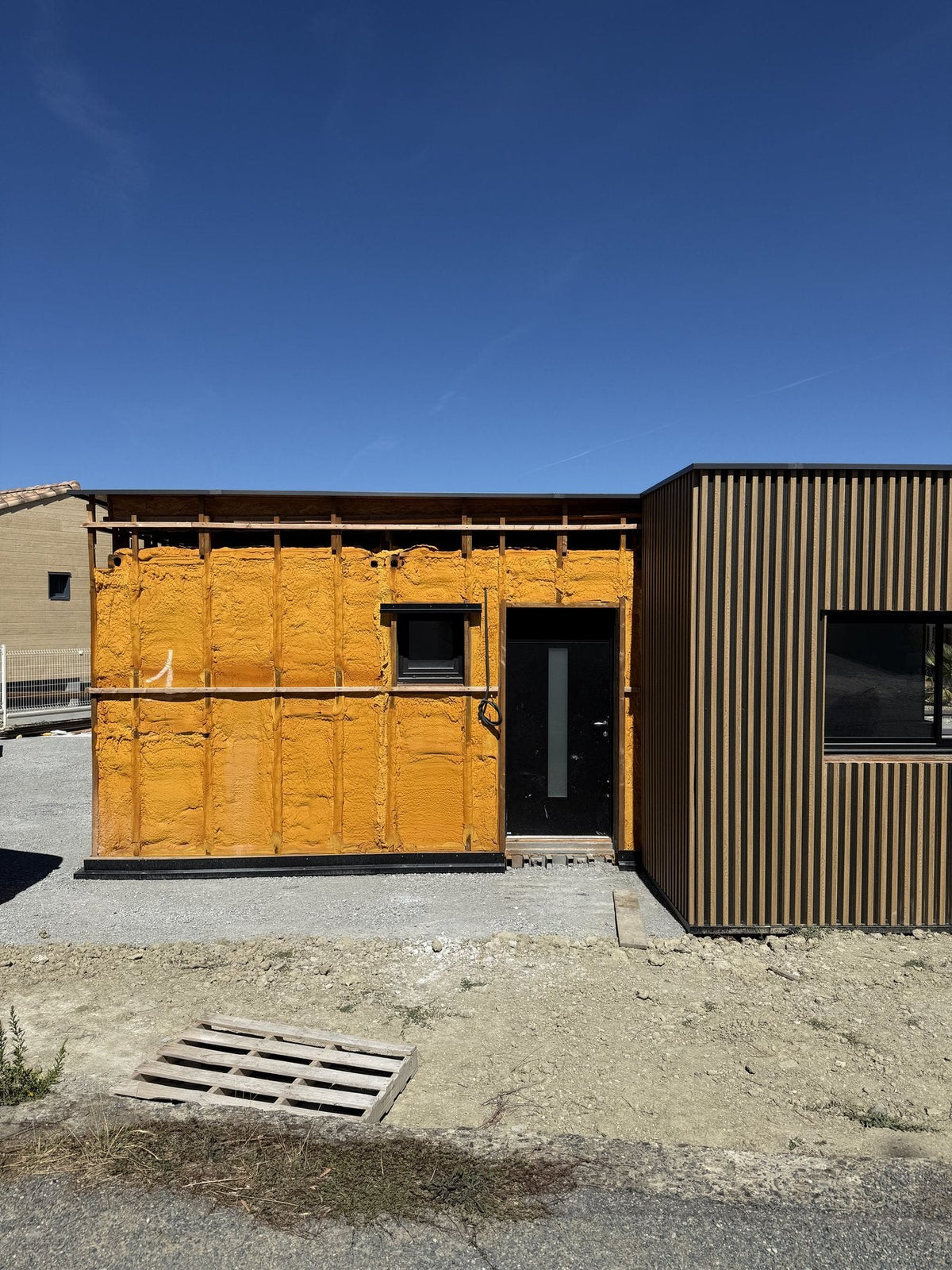 Mur de maison container entièrement enveloppé d'isolant par l'extérieur avant la pose du bardage, ce qui protège l'acier et fonde sa durée de vie