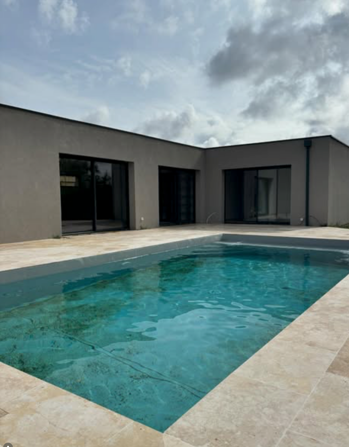 Maison container de plain-pied à Teulat, façade enduite grise et menuiseries noires, terrasse et piscine au premier plan