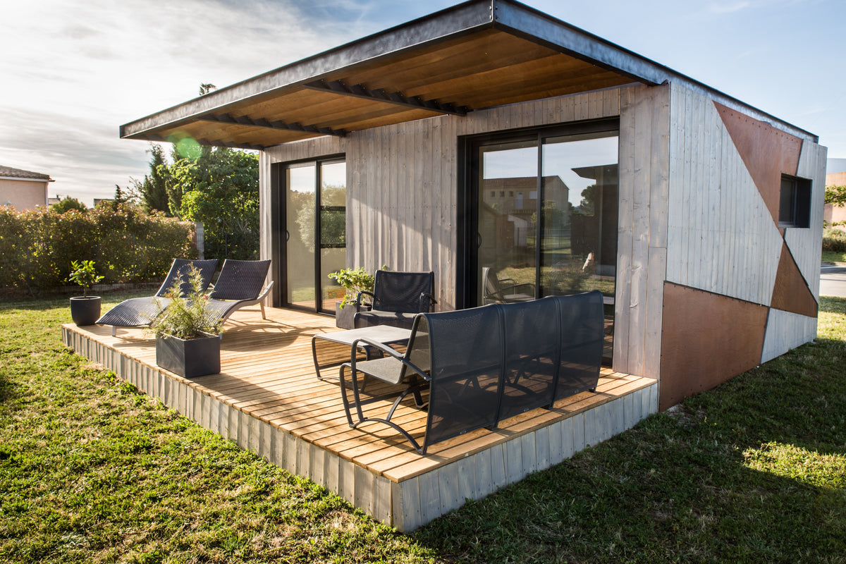 Maison conteneur de plain-pied avec sa terrasse en bois, façade claire et grandes baies vitrées à menuiseries noires