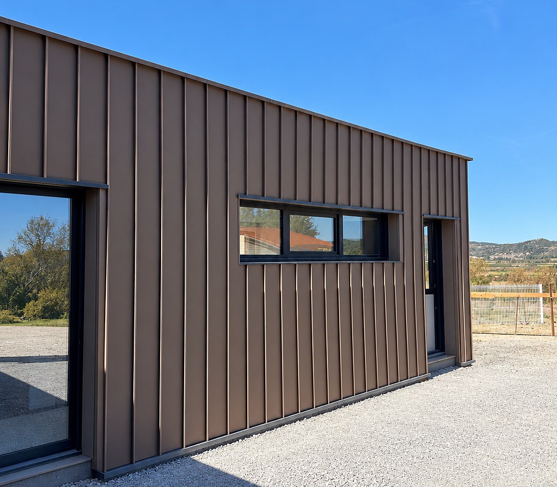 Bâtiment à bardage métallique brun à joints debout, baie vitrée toute hauteur et fenêtre bandeau, projet mené avec MO|OM architectures, l'agence de Myriam Carde