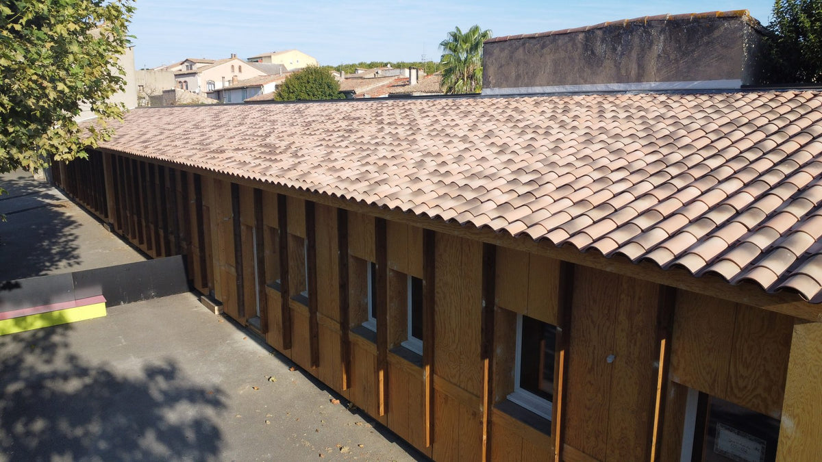 Vue aérienne du bâtiment en containers maritimes de l'école catholique Saint-Michel à Carcassonne, bardage bois à tasseaux verticaux et toiture en tuiles canal, en secteur sauvegardé